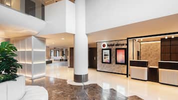 Un hall d’hôtel moderne avec un comptoir d’accueil, un espace salon et une grande plante.