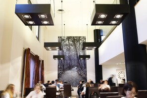 A modern interior with multiple seating areas, a large wall-mounted artwork depicting a forest path, and contemporary lighting fixtures. - Hotel Alimara (Barcelona)