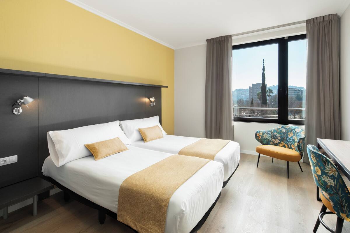 A hotel room with two beds, a desk, and a chair.