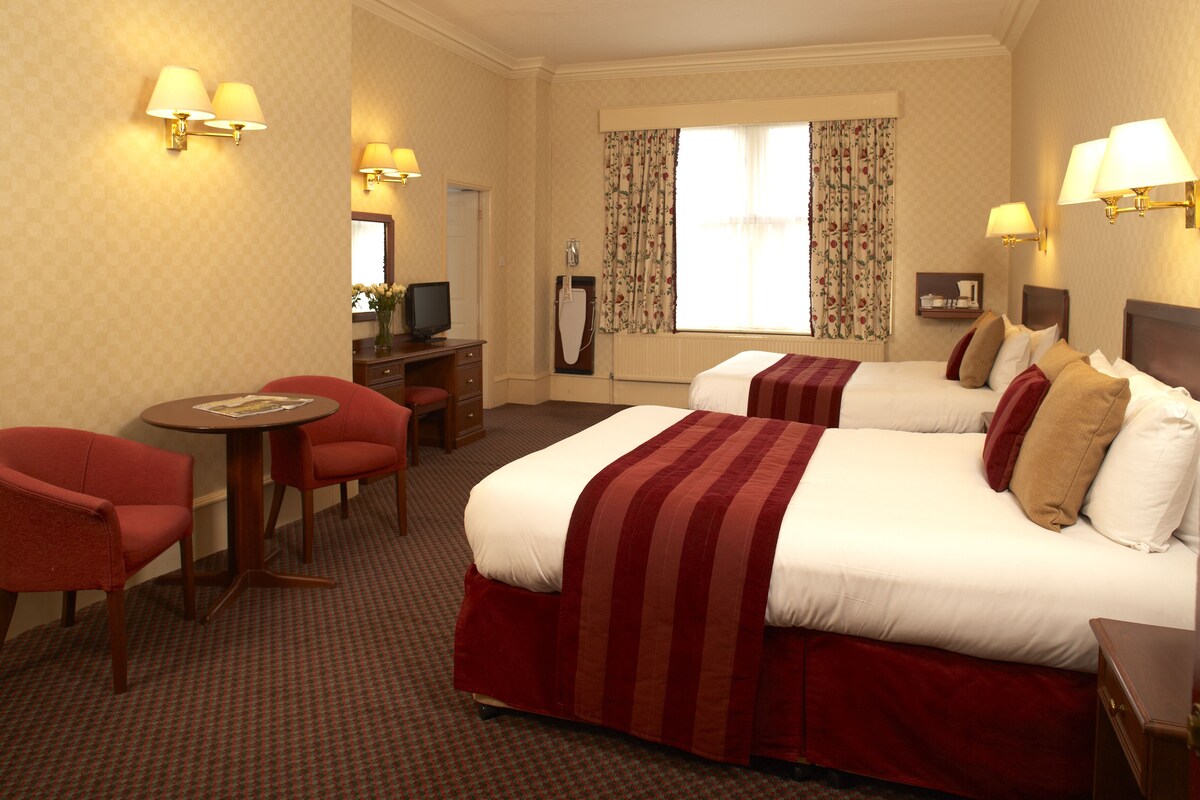 A hotel room with two beds, a desk, a chair, and a television.
