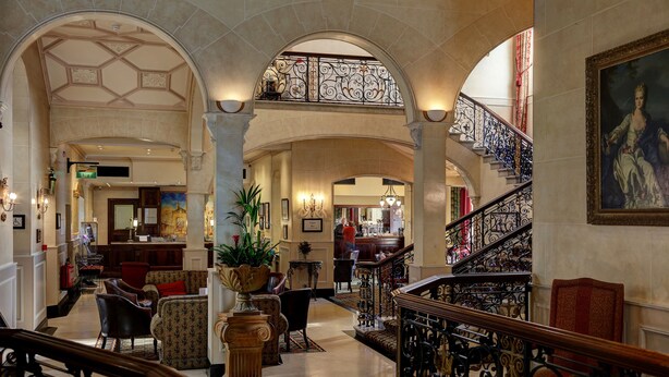 Un amplio vestíbulo con techo alto, barandales de hierro ornamentados y una escalera que conduce a un nivel superior.