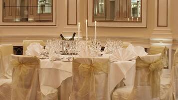 A formal dining room with a table set for a meal, surrounded by chairs with white covers and bows.