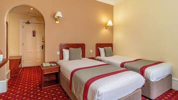 Quarto de hotel com duas camas, uma escrivaninha, um telefone e uma luminária.