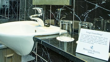 Ein Badezimmer mit einem weißen Waschbecken, schwarzen Marmorfliesen und einem Hinweis zu vergessenen Gegenständen.