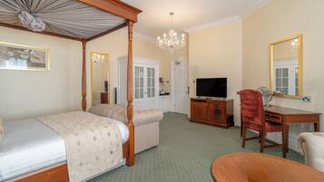 A bedroom with a four-poster bed, a sitting area, a television, a desk, and a mirror.