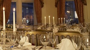 Un comedor formal con varias mesas dispuestas para una comida, cada una con velas y porcelana fina.