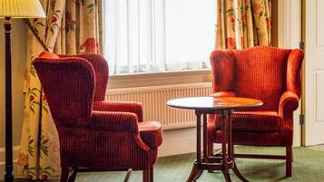 A room with two red upholstered chairs and a small round table, a floor lamp, and floral curtains.