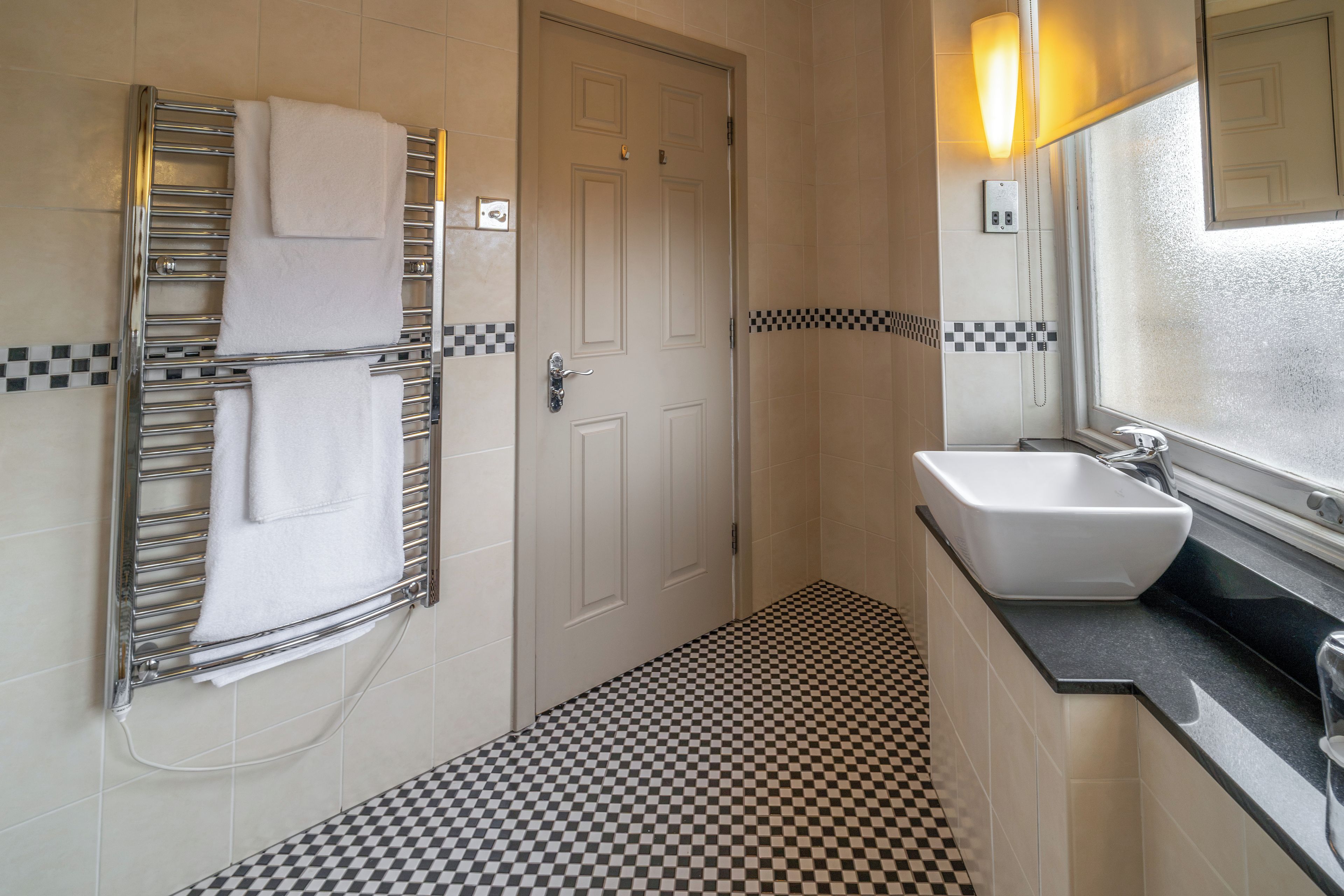 A bathroom with a checkered floor, a towel rack, a sink, and a door.