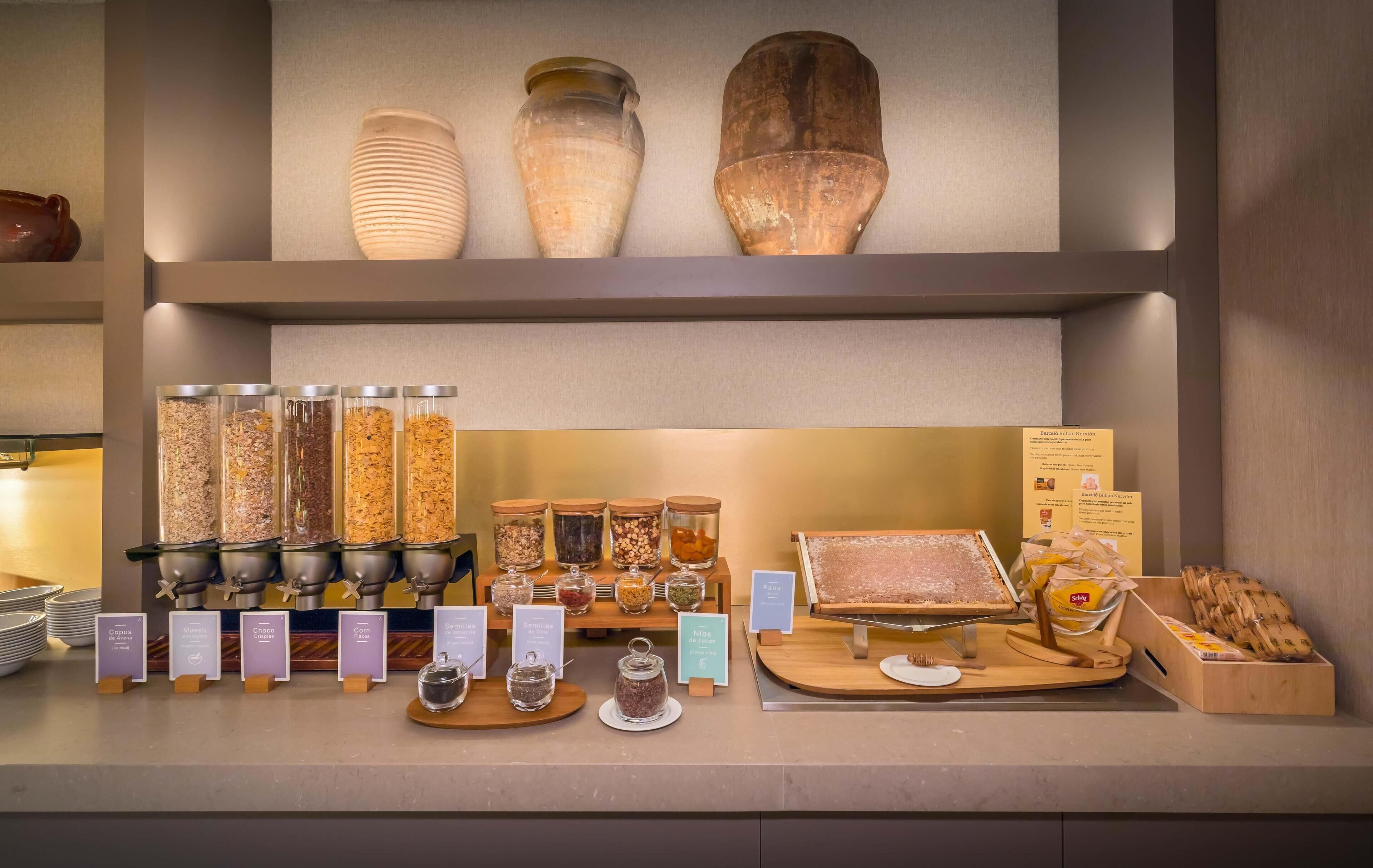 A food display with various jars of grains and nuts, a bread display, and a wooden cutting board with a knife.