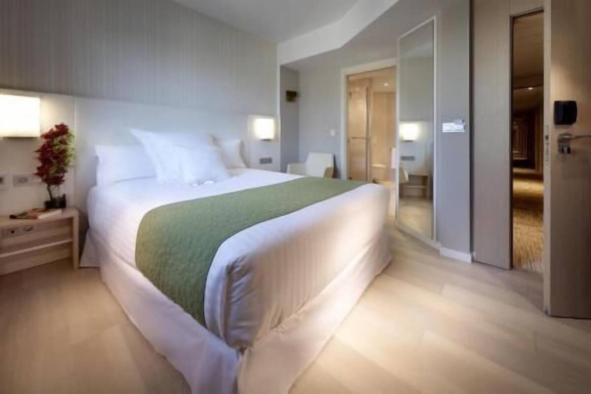 A modern hotel room with a large bed, bedside tables, a green throw blanket, and a walk-in closet.