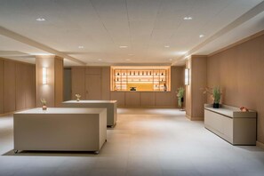 A modern hotel lobby with a central reception desk, a seating area, and a wall-mounted display case.
