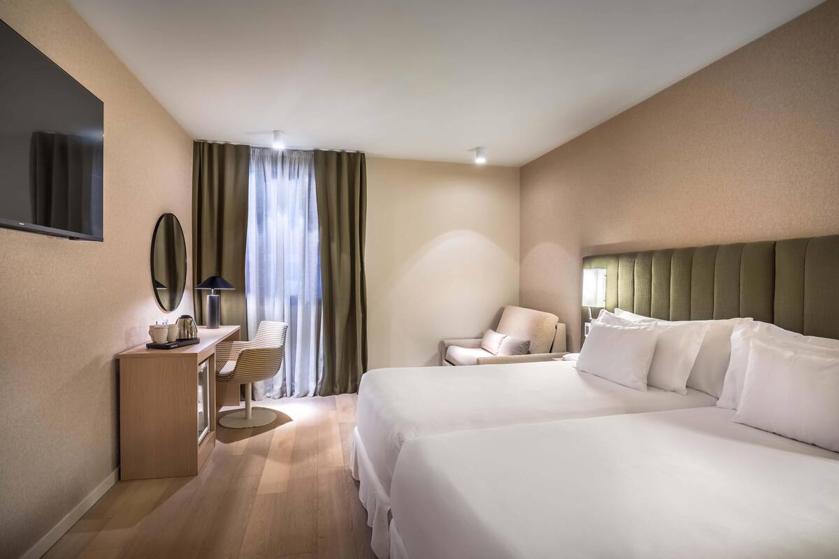 A hotel room with a large bed, a desk with a chair, a television, and a window with curtains.