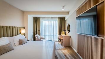 Une chambre d’hôtel avec un grand lit, un bureau, une chaise, une télévision et une fenêtre avec des rideaux.