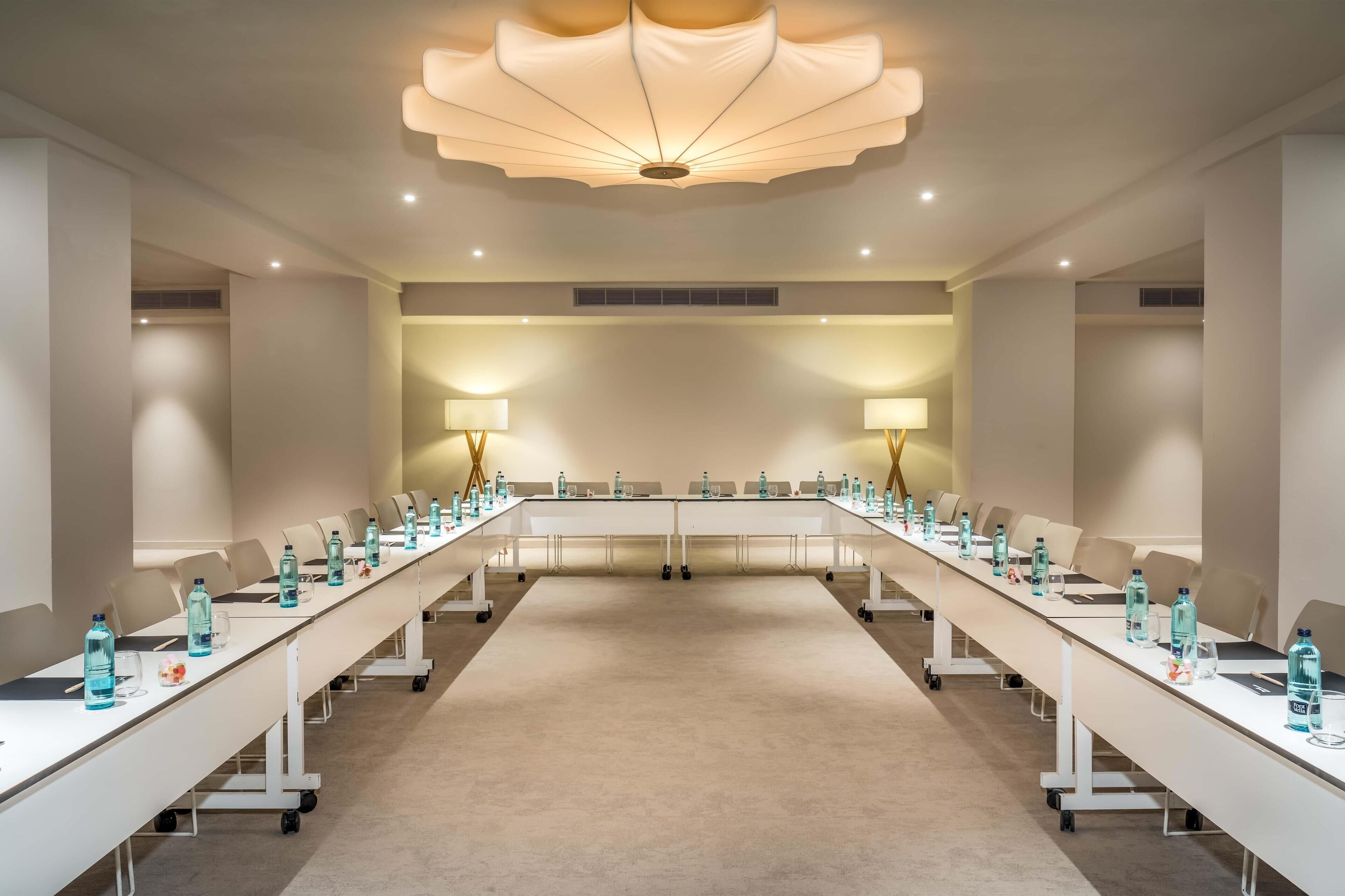 A conference room with a long table, chairs, water bottles, and lamps.
