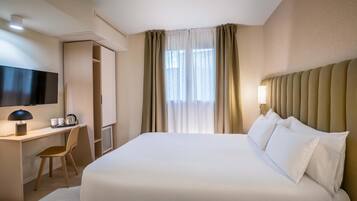 Una habitación de hotel con una cama grande, un escritorio con silla, televisión y ventana con cortinas.