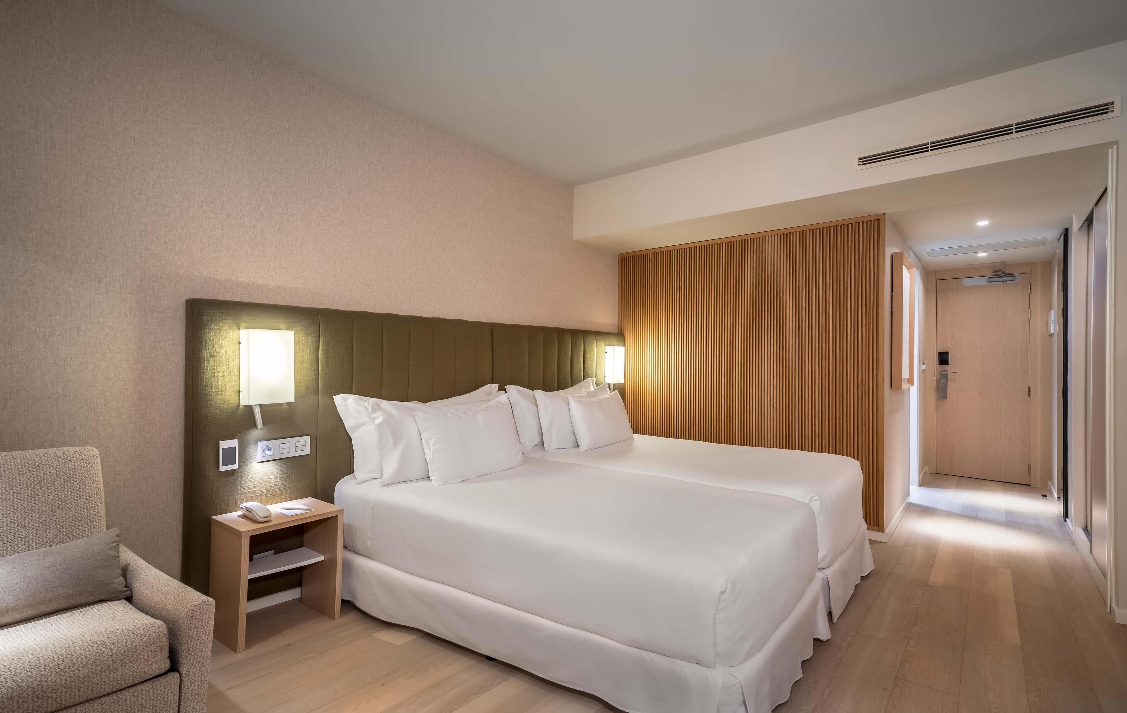 A hotel room with a large bed, bedside tables, a chair, and a wooden panel wall.