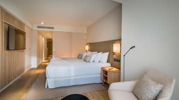 Una habitación de hotel moderna con una cama grande, mesitas de noche, un televisor de pantalla plana y una zona de estar con una silla.