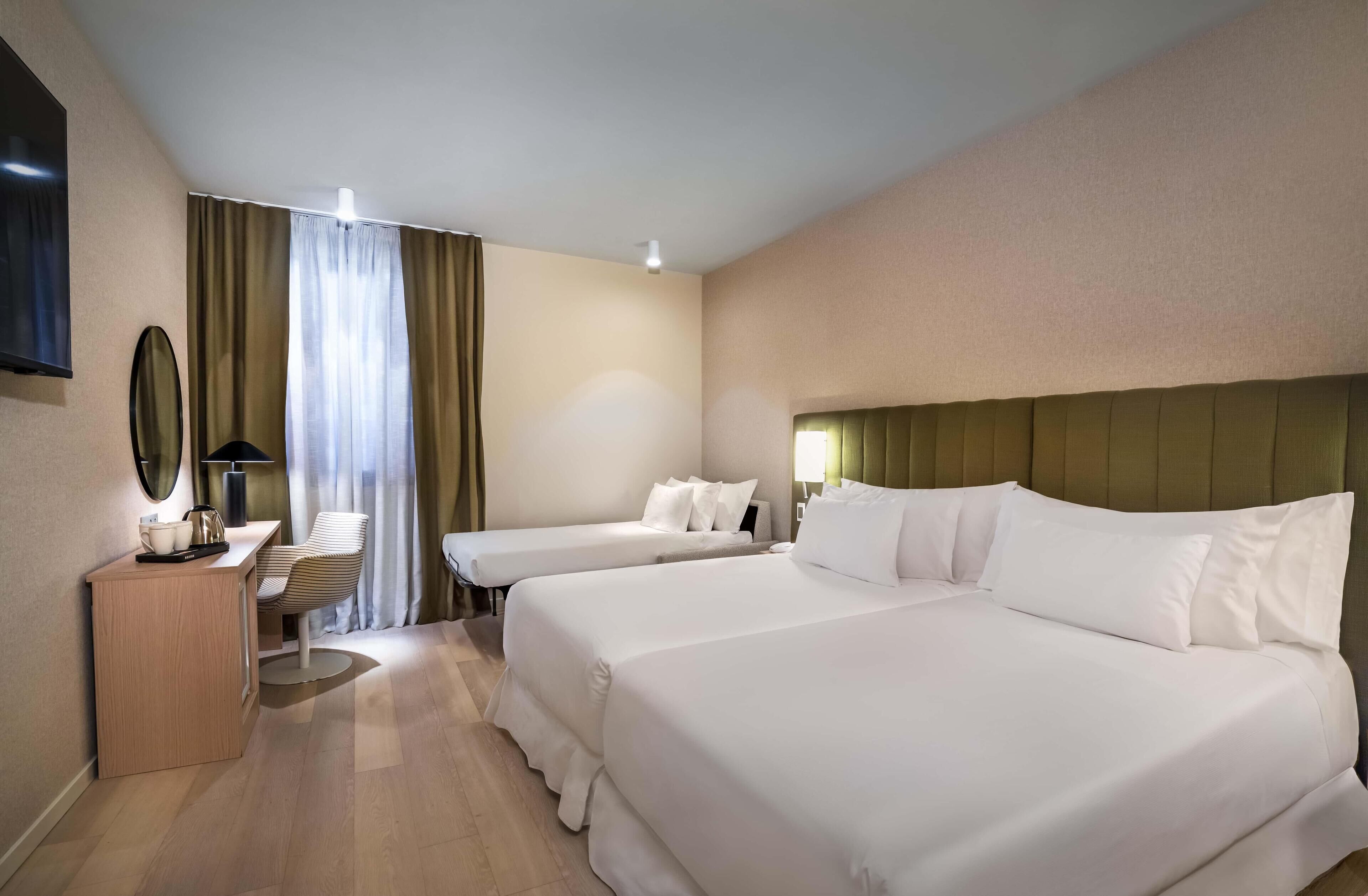 A hotel room with two beds, a desk with a lamp, a mirror, and a view of the outdoors through curtains.