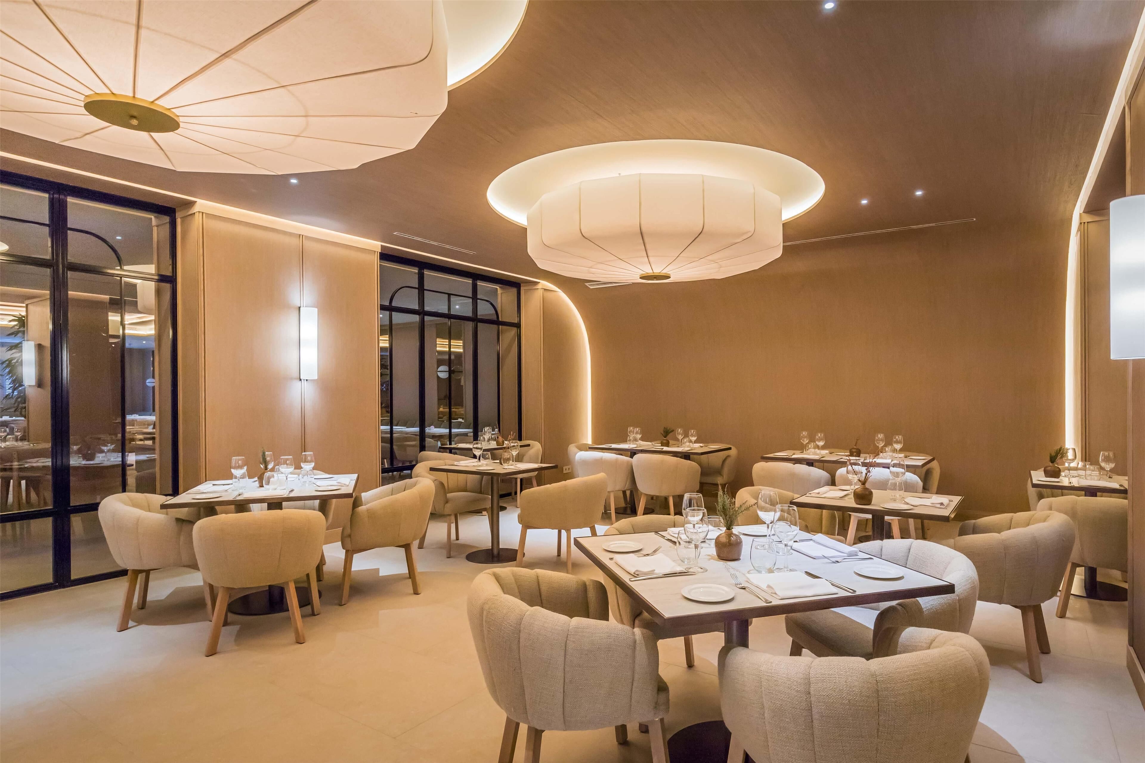 A modern dining area with round tables, beige chairs, and ambient lighting.