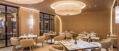A modern dining area with round tables, beige chairs, and ambient lighting.