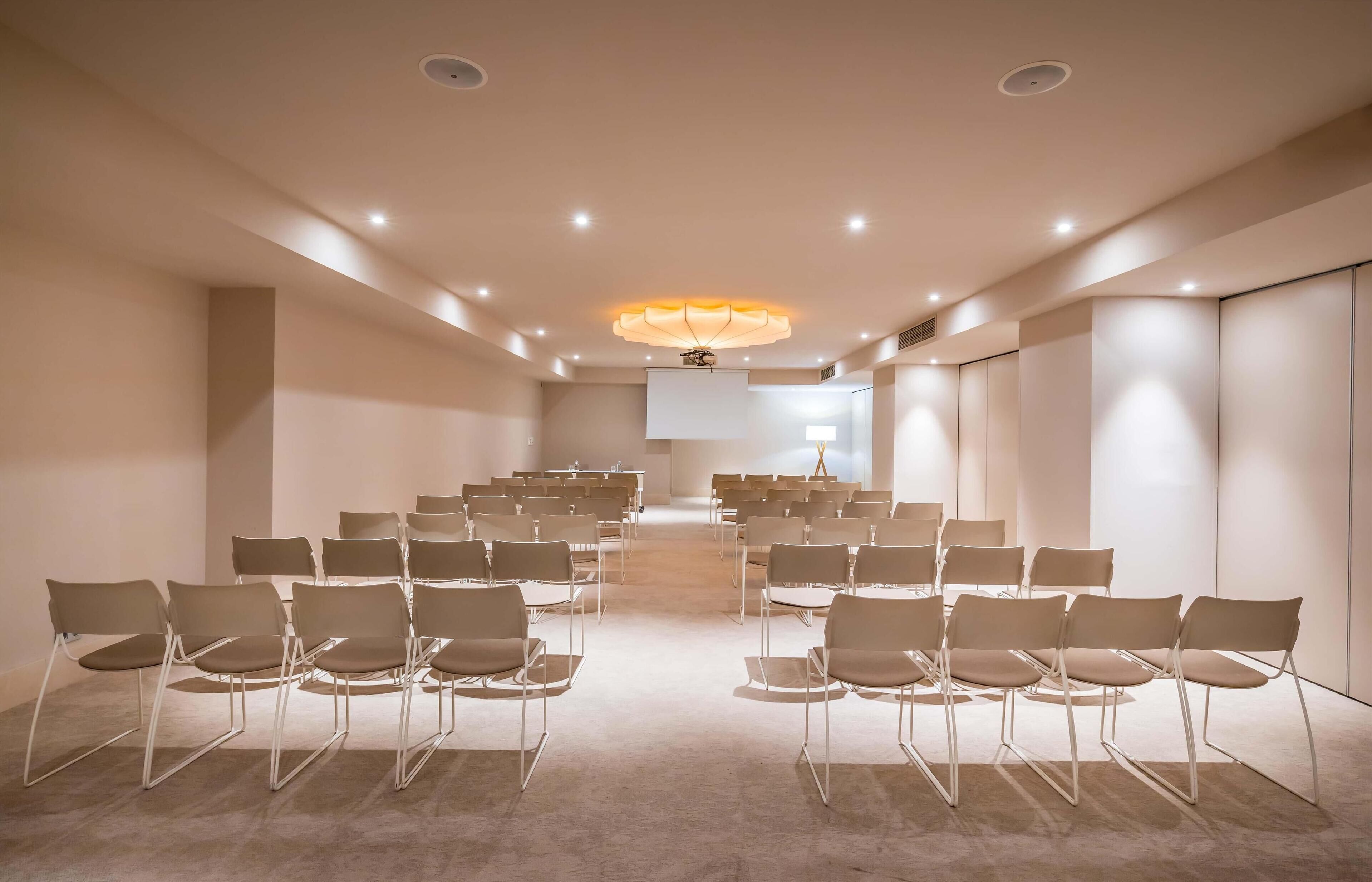 Una sala de conferències amb files de cadires, una pantalla gran i una làmpada de cristall moderna.