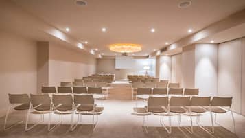 A conference room with rows of chairs, a large screen, and a modern chandelier.