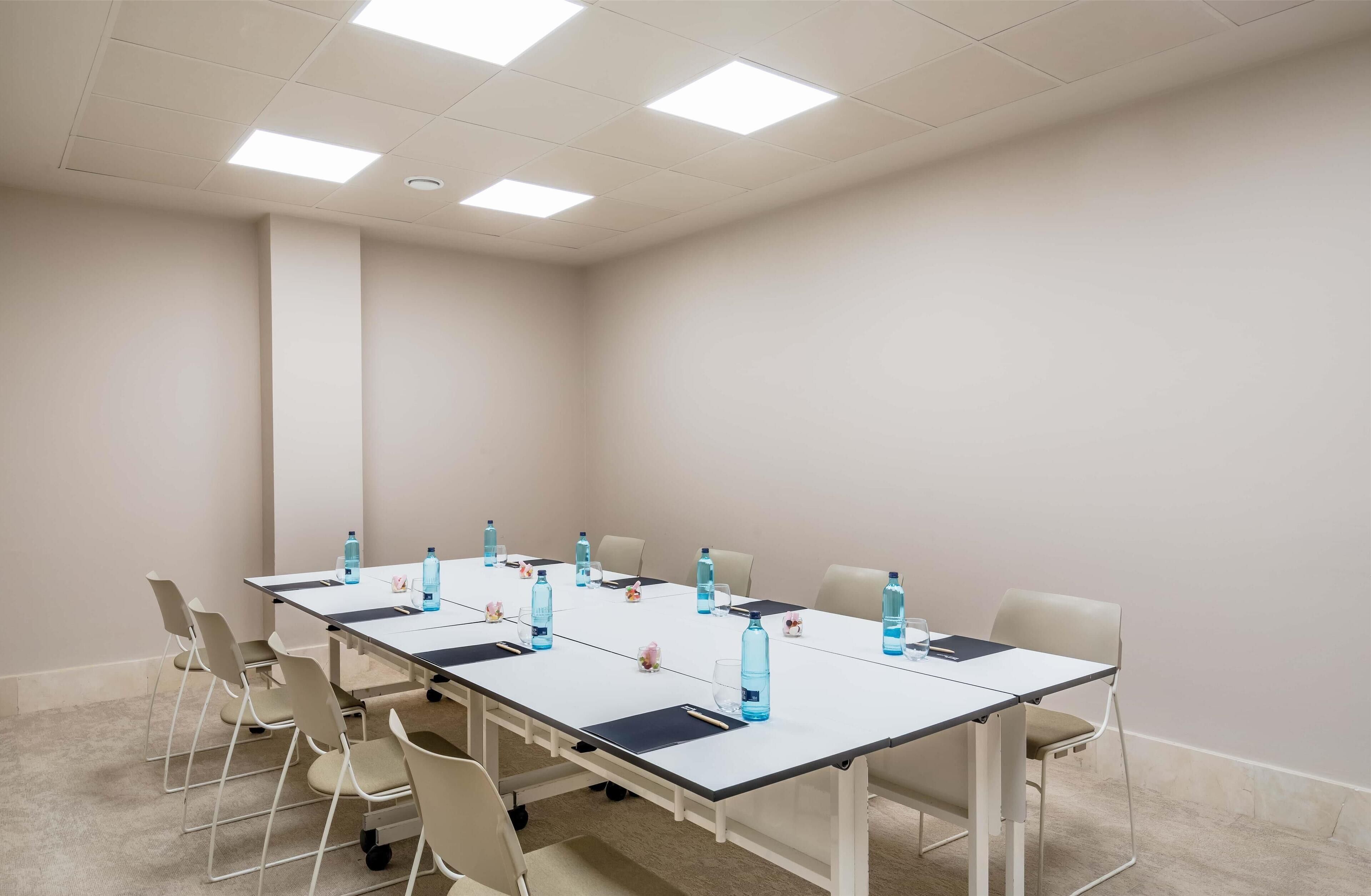Une salle de conférence avec une longue table, des chaises et des bouteilles d’eau.
