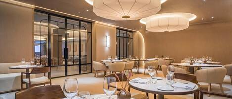 Un comedor moderno con mesas redondas, sillas y una lámpara de techo circular grande.