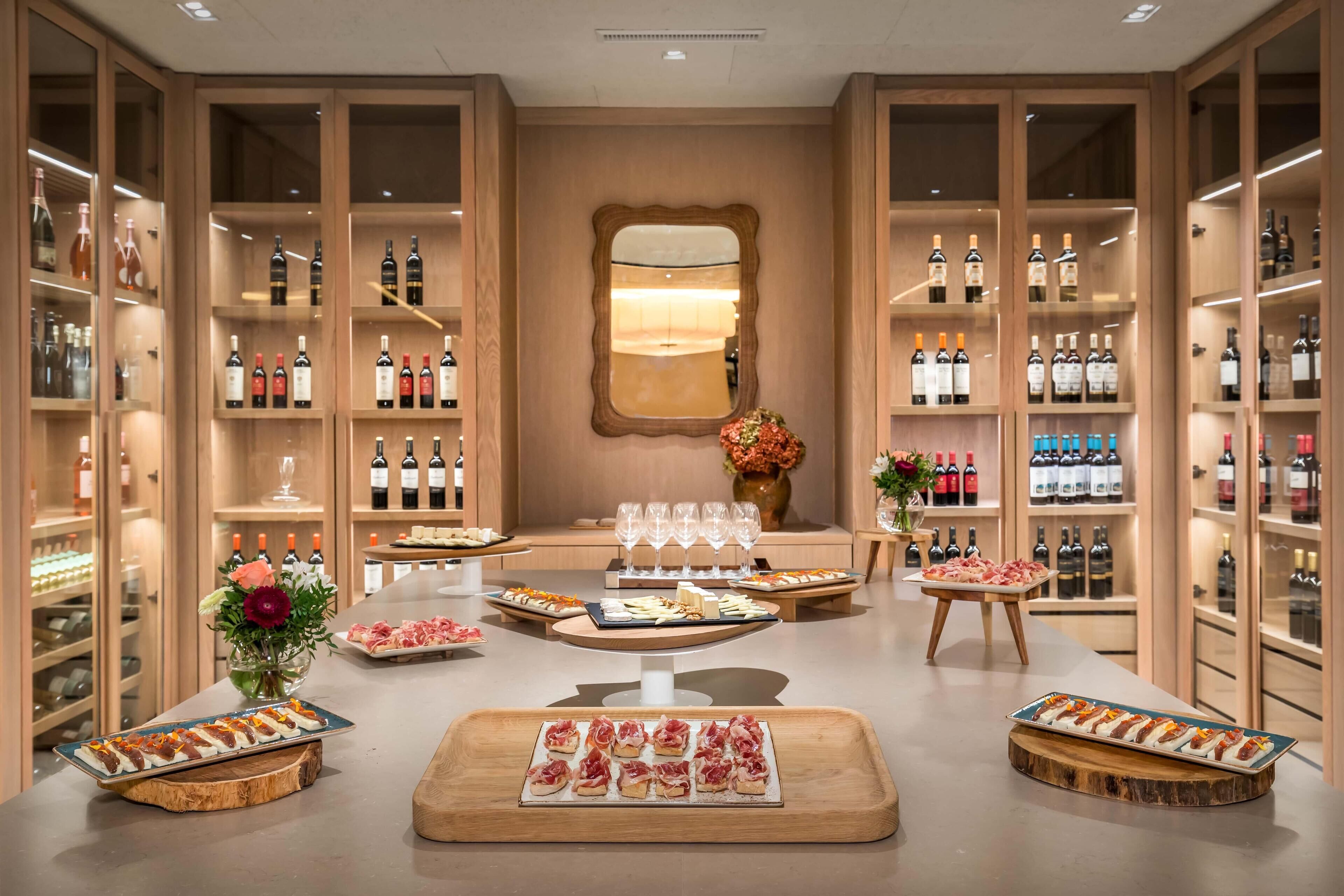 Une salle de dégustation de vins avec des étagères en bois, des bouteilles de vin, des verres et des plateaux de nourriture.