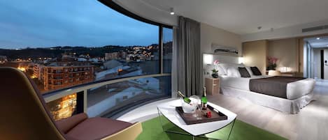 Una habitación de hotel moderna con un balcón curvo, una cama, un sofá y una mesa de centro con una botella y vasos.