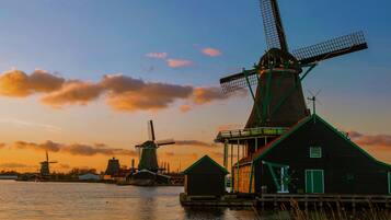 Een traditionele windmolen en houten gebouwen bij een waterlichaam tijdens de zonsondergang.