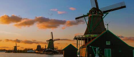 A traditional windmill and wooden structures by a water body during sunset.