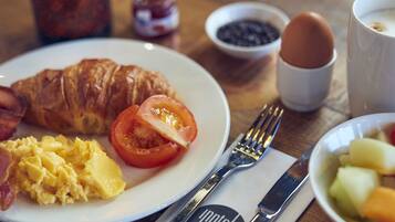 A breakfast plate with croissant, bacon, scrambled eggs, and tomato.