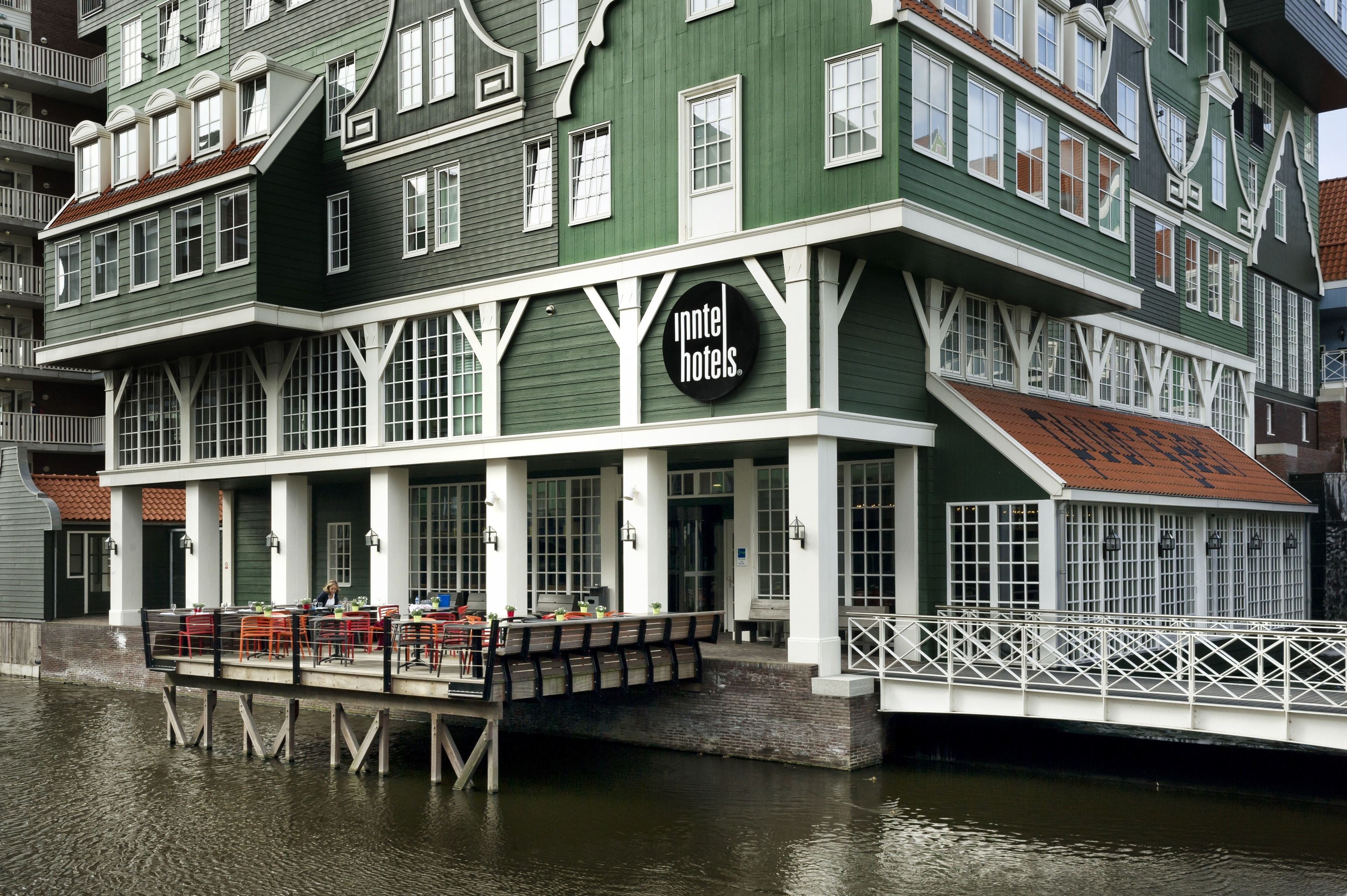 A green building with a sign reading "Intel Hotels." It features a covered outdoor seating area with tables and chairs.