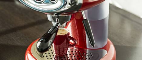 Una máquina de café espresso roja y blanca con un recipiente para café y una taza.