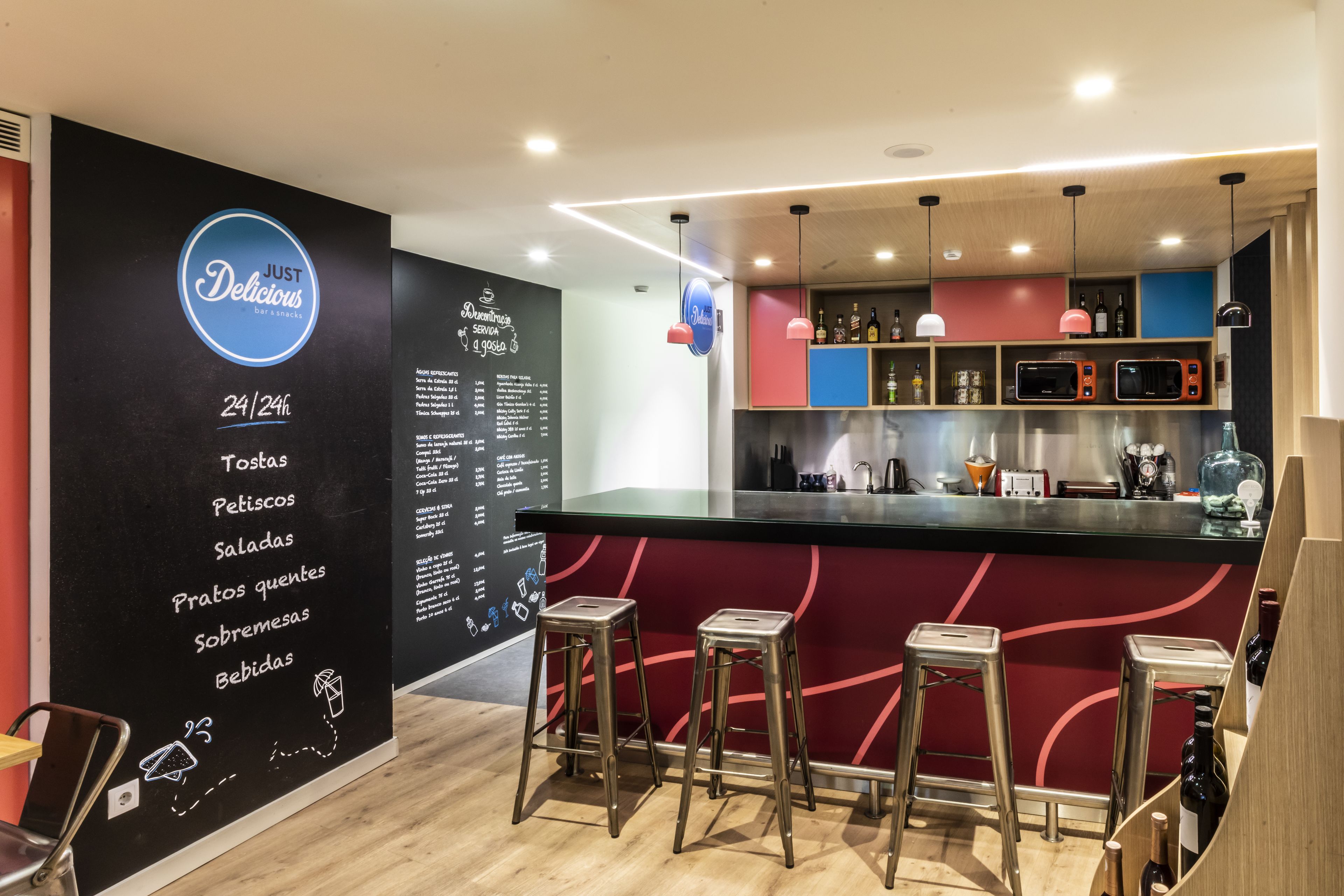 A bar area with stools, a menu on the wall, and a counter with bottles and glasses.