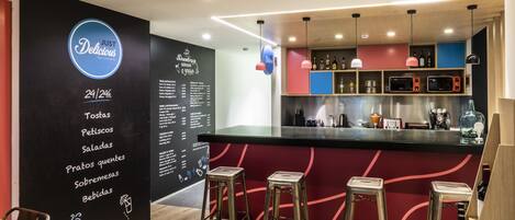 A bar area with stools, a menu on the wall, and a counter with bottles and glasses.