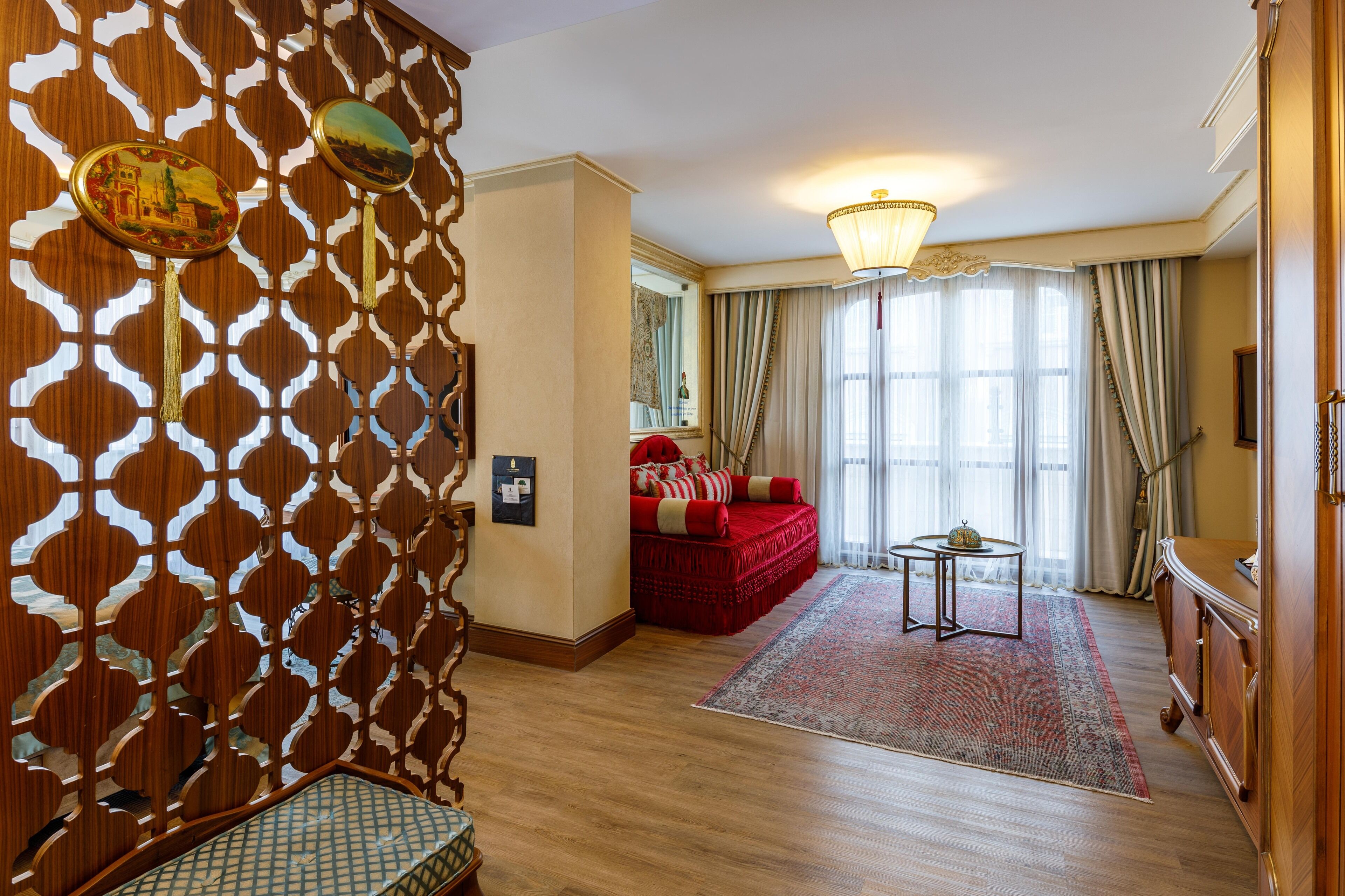 Una habitación con un separador de madera decorado, un sofá rojo, una mesita redonda y un candelabro.