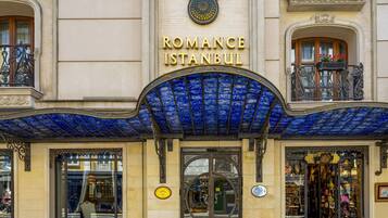 El exterior del hotel Romance Istanbul, con un dosel de entrada en azulejos azules, intrincada herrería y un cartel llamativo sobre la entrada.