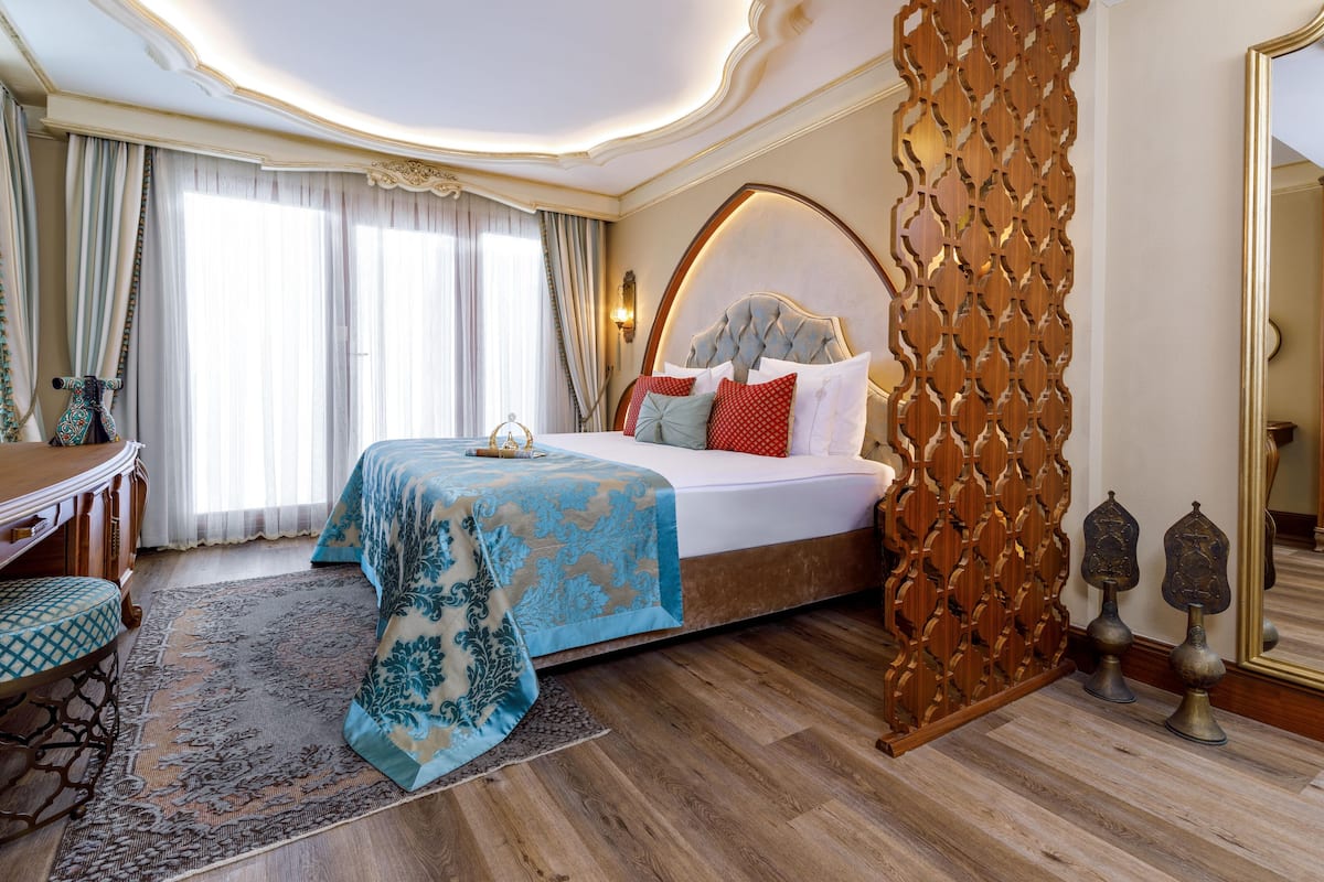 A bedroom with a large bed, a wooden headboard, a decorative wall panel, and a mirror.