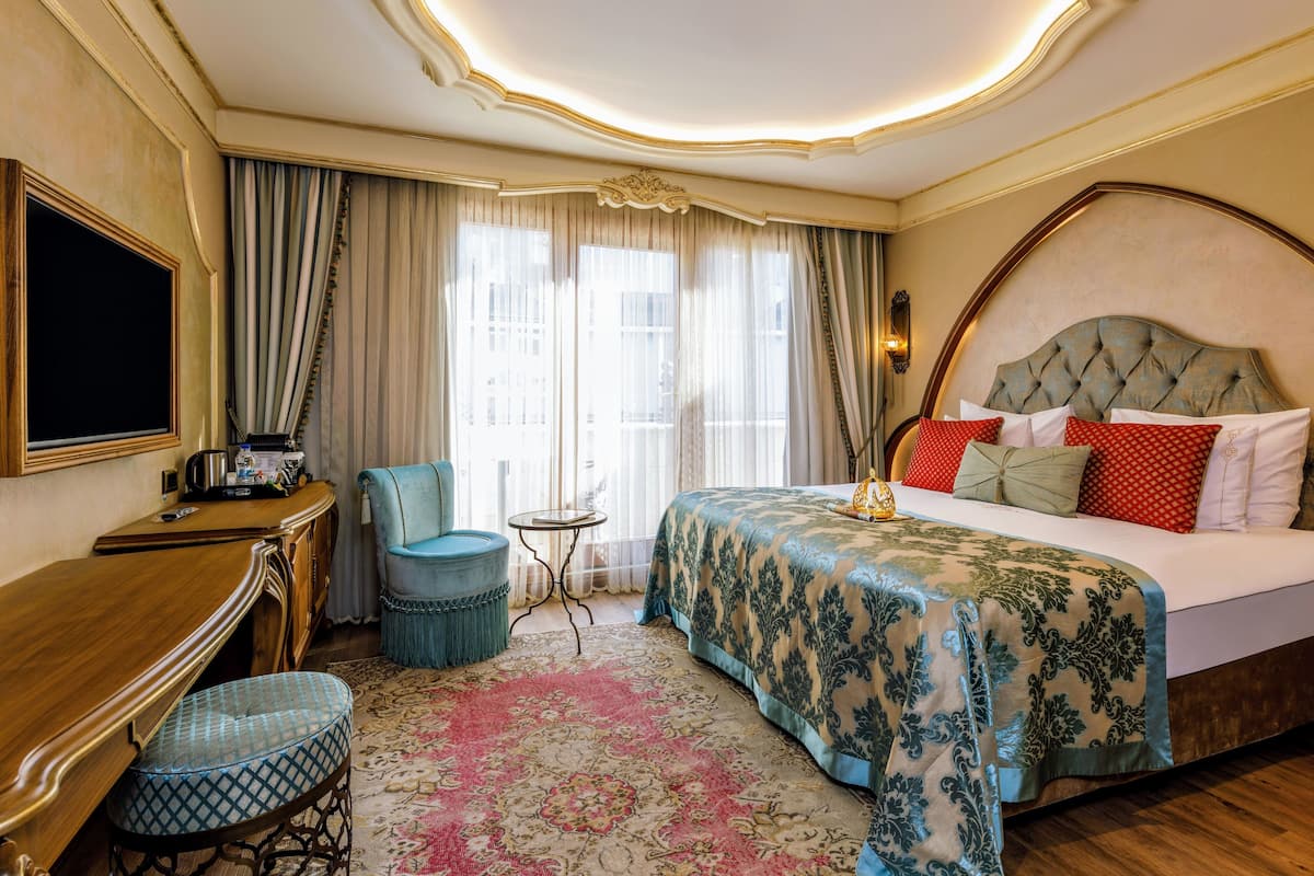 A hotel room with a large bed, a desk with a chair, a small round table, and a TV.