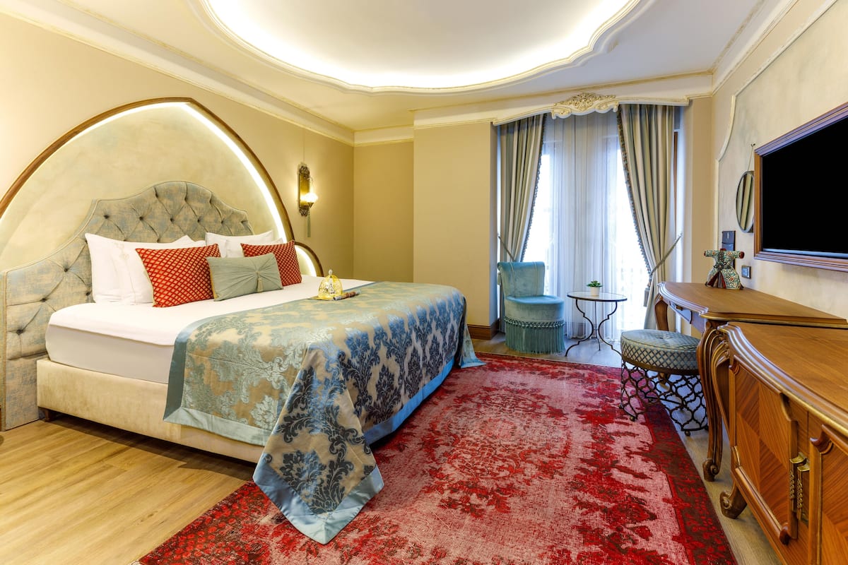 A spacious bedroom with a large bed, a wooden dresser, a small table, and a television.