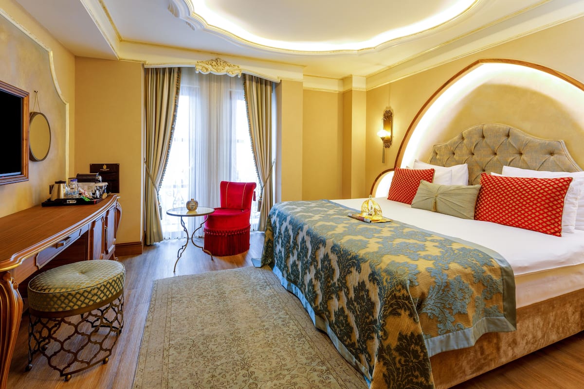 A hotel room with a large bed, a red armchair, a small round table, and a television on a wooden cabinet.
