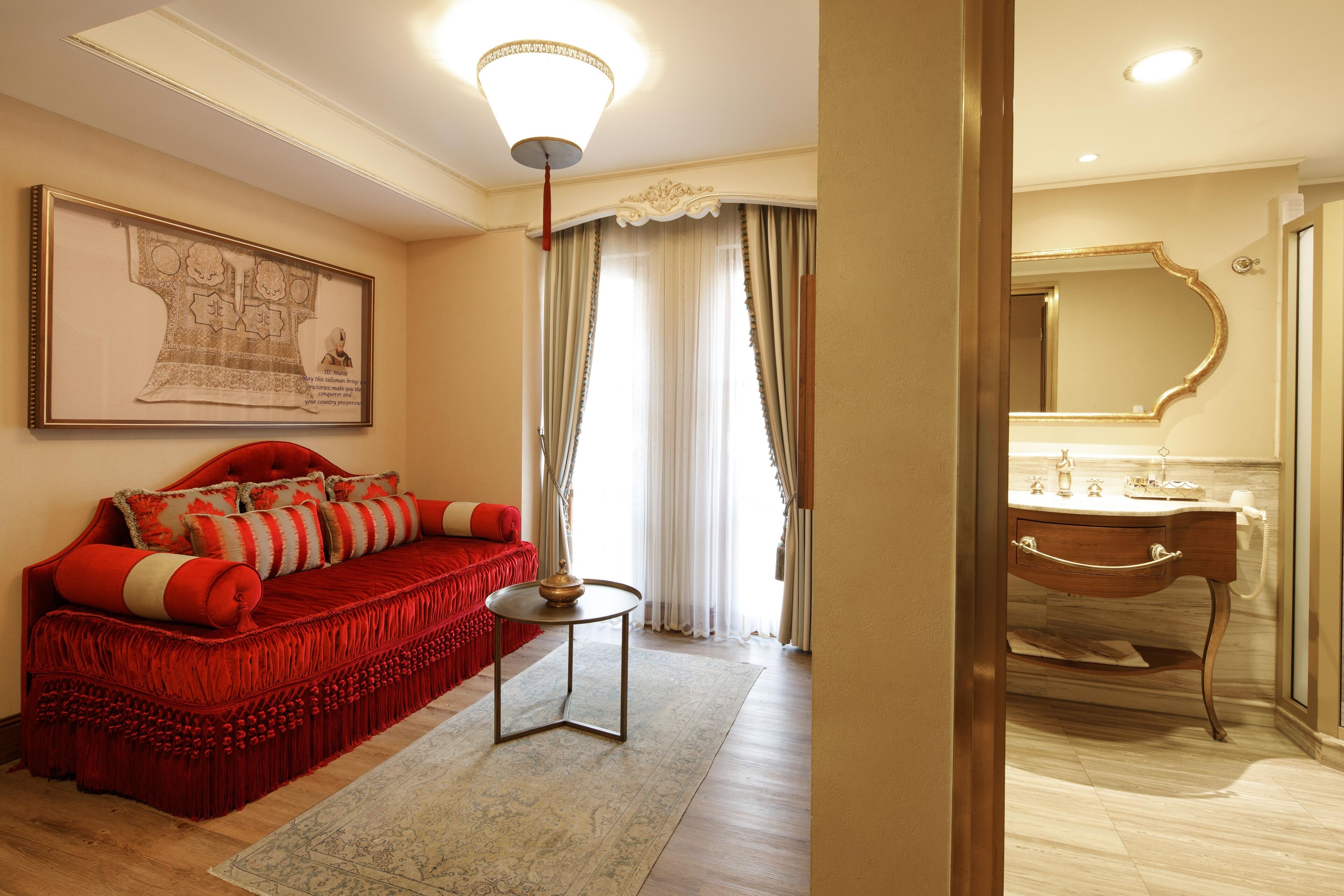 A well-lit room with a red sofa, a small round table, a framed map on the wall, and a bathroom with a mirror and sink.