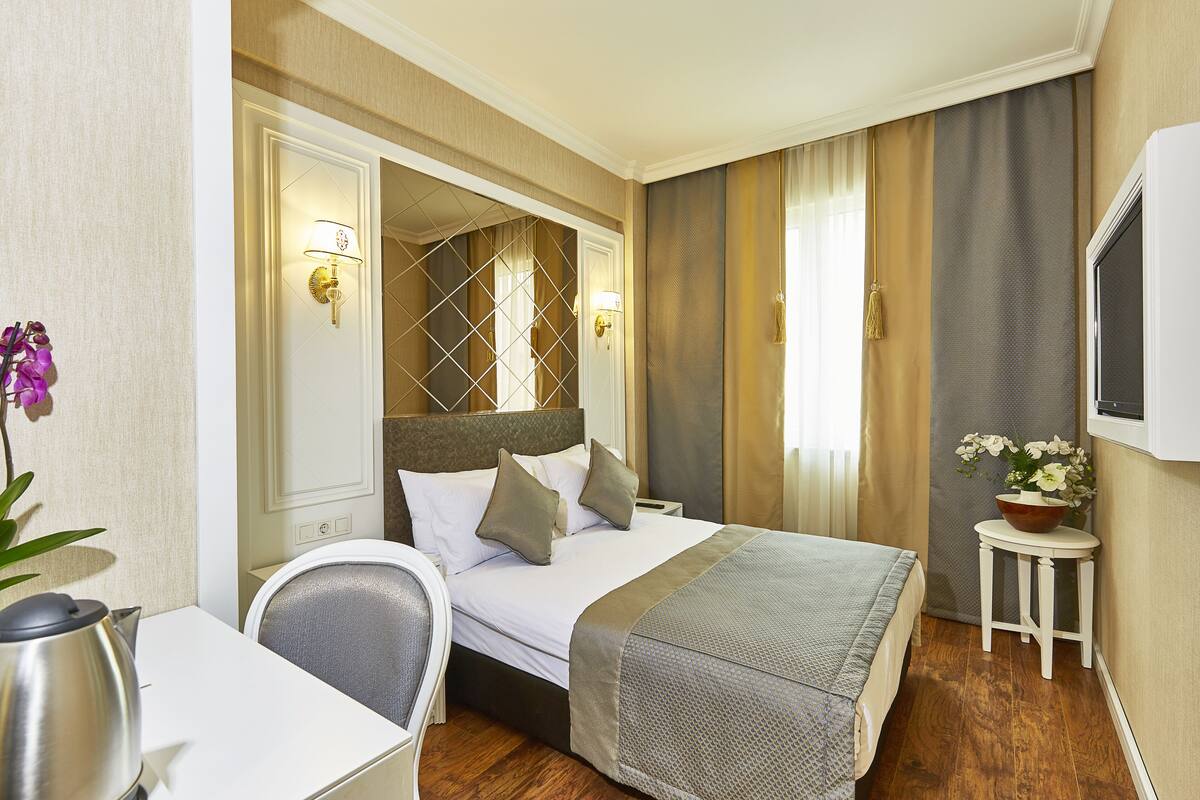 Habitación de hotel con cama, mesita de noche, silla y una pequeña mesa con un florero.