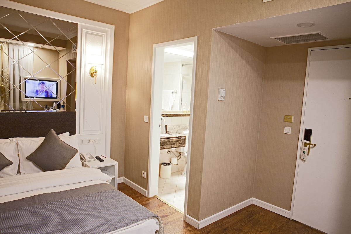 Habitación de hotel con cama, televisor en una mesita de noche, baño visible a través de una puerta abierta y una puerta con cerradura de llave electrónica.