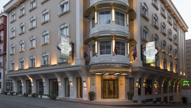 A multi-story hotel with a prominent curved corner, a sign reading "Olive Olive Restaurant," and multiple flags. - Hotel Yasmak Sultan (Istanbul)