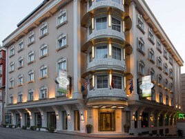 Un edificio histórico con entrada en esquina, múltiples ventanas y banderas.