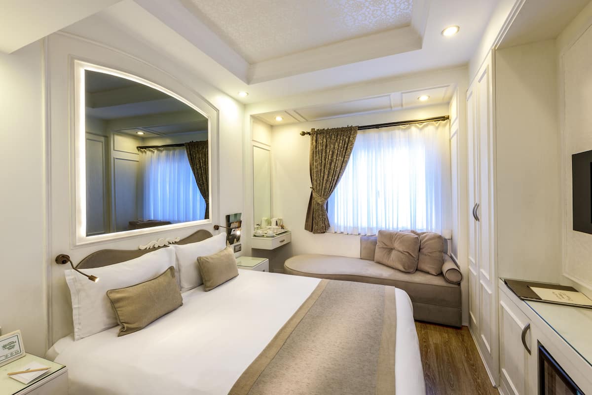 A hotel room with a large bed, a sofa, a desk, and a TV.