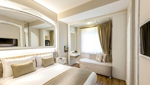 Habitación de hotel con una cama grande, un sofá, una mesita de noche, un espejo y una ventana con cortinas.